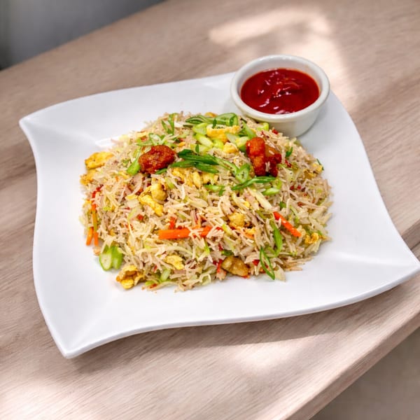 Fried rice with chicken, egg, vegetables, and a side of red chili sauce on a white plate.