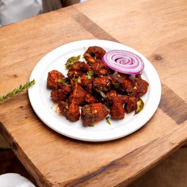 Spicy chicken fry with red onion and herbs on a white plate, on a wooden table.