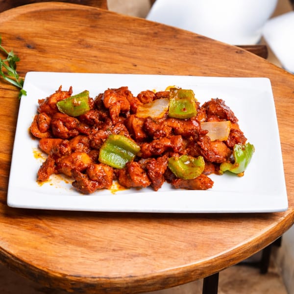Spicy chicken with green bell peppers and onions on a white rectangular plate.