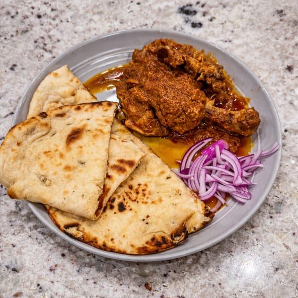 A plate of chicken curry with naan bread and sliced red onions on a speckled countertop.