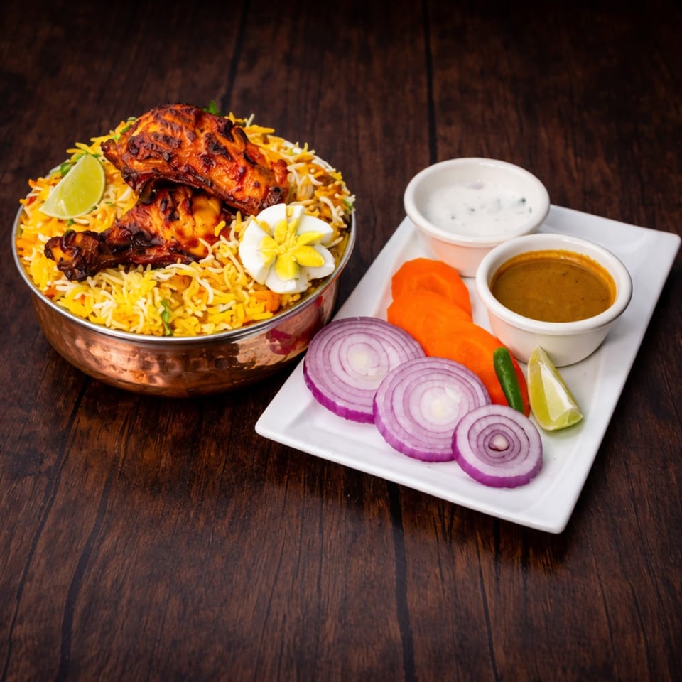 Chicken biryani in a copper pot with lime, egg, and a side of sauces and vegetables.